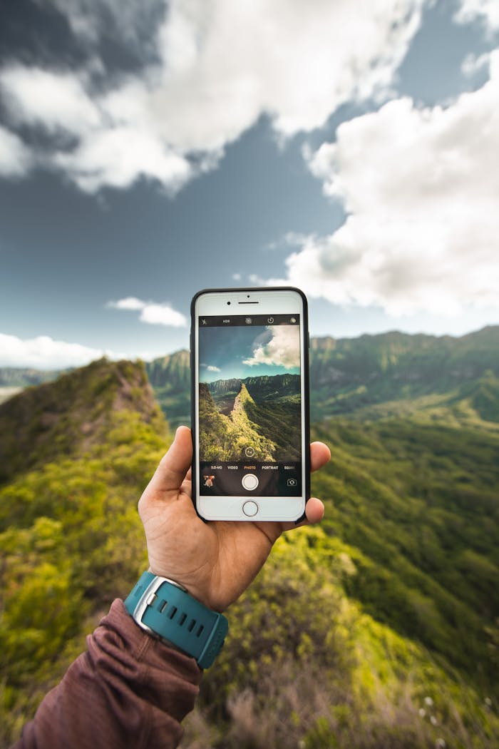 A person captures scenic mountains on a smartphone during a daytime hike.