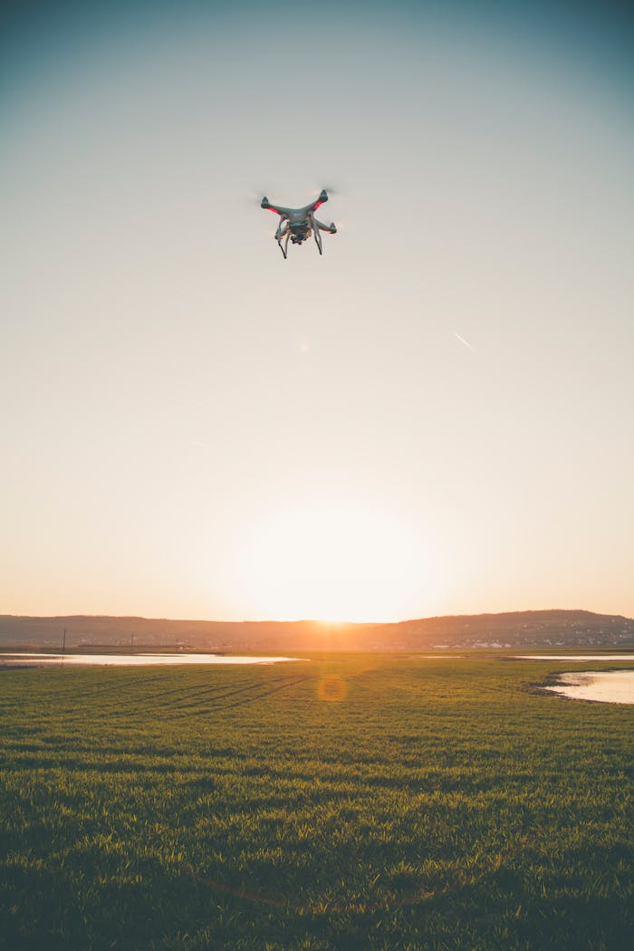 A drone flies over a tranquil landscape at sunset, capturing lush green fields and a serene horizon.